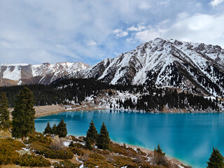 Stunning turquoise lake surrounded by snowy mountains and evergreen trees in the Kazakh landscape