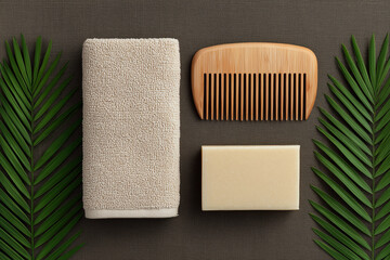 Natural spa and grooming flatlay with towel soap bar wooden comb and palm leaves on brown fabric