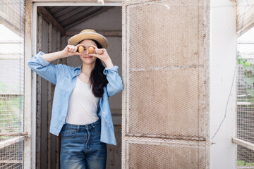 Young generation Z woman on farm holds eggs playfully over her eyes enjoying agricultural education outdoors with happy and relaxed expression in rural setting