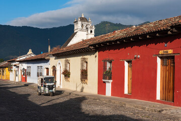 Tuc tuc taxi rides on an empty street next to a red house