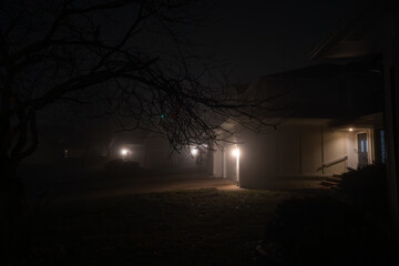 Lights illuminate driveway and entrance of house on a foggy night