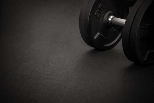 Black dumbbell resting on dark gym floor after strength training