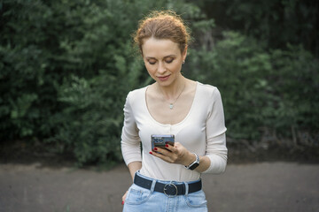 Woman in park using her phone, smiling and texting.