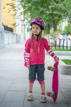 A little girl with pink skateboard in the park.