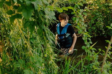 Boy exploring lush creek wearing life jacket