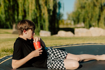 Boy lounging on trampoline sipping drink in red cup outdoors