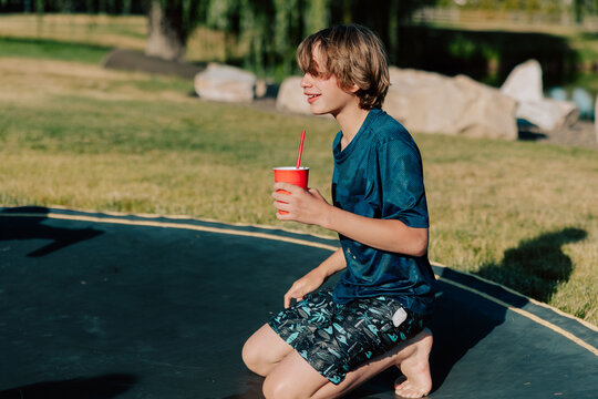 Teen boy kneeling on trampoline drinking from red cup
