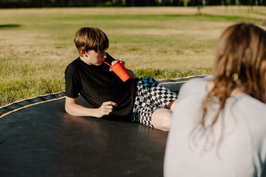 Teen boy lying on trampoline drinking with straw in backyard
