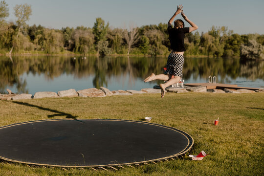 Boy jumps mid-air near trampoline by a scenic lakeside