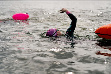 Woman in wetsuit with buoy swimming across lake, open water training