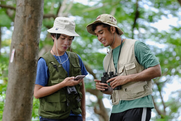 Bird watching is recreational pursuit. Young man and friend have fun with outdoors leisure activity looking up for bird in nature public park. Gay couple enjoy using binocular for bird watch adventure