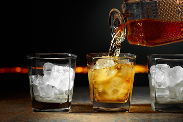 Whiskey is poured from a decanter into a glass with ice.