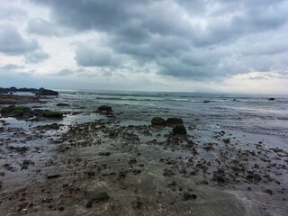 Cloudy skies hung over the beach with the water receding against the rocks
