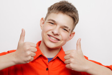 Smiling teenager with braces showing thumbs up, dental care and orthodontics concept