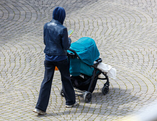 A woman is walking with a baby stroller and a cell phone in her hand