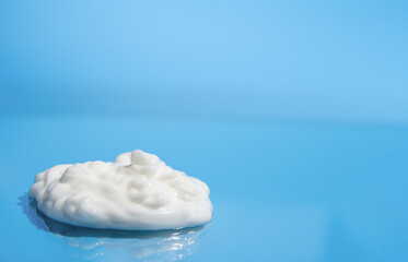 White cream on a blue background. A dollop of white cream rests on a shiny, blue surface. The...