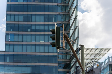 A green traffic light hangs in front of a modern high-rise with a glass facade. The cityscape shows...