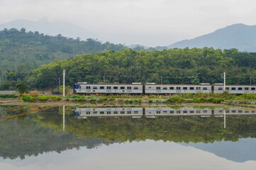 Obraz premium Rural Charm: Train Journey Through Verdant Fields and Hazy Mountains.