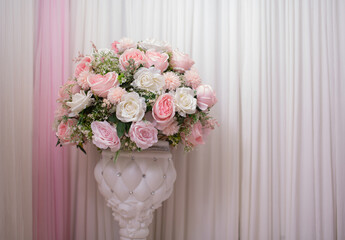 White potted plant with pink and white roses on the background of white wavy curtains as a copy space.