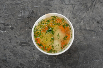 Chicken soup in a disposable container on a gray background