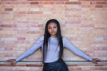 African woman, young and beautiful dressed in beige top and black leather shorts leaning on a red...