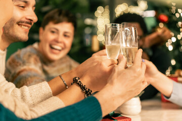 A close-up of a diverse group of friends' hands clinking champagne glasses in a toast, with their laughing faces blurred in the background during a festive Christmas celebration.