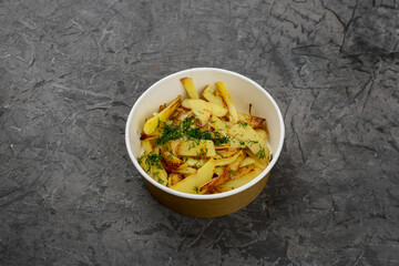 fried potatoes with herbs in a disposable dish on a gray background