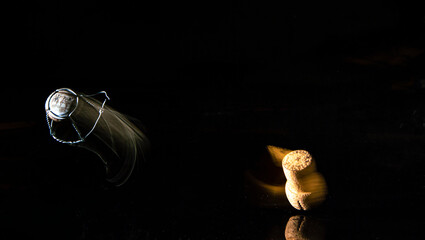 Tapón de corcho de una botella de cava saltando, dejando una estela con fondo negro.