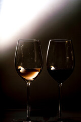 Fotografía de dos copas de vino blanco y tinto con fondo negro y luz lateral.