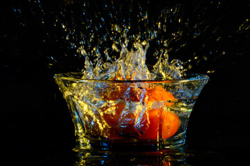 Albaricoques cayendo dentro de un bol transparente, salpicando el agua con fondo negro y destellos azules. 