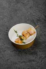 fried kebab on a wooden skewer in a disposable dish on a gray background