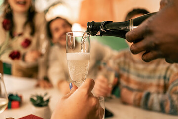 Close-up of pouring champagne in a glass with bubbles at a festive party. A group of friends celebrate New Year's Eve or a holiday with a toast of sparkling wine at home or in a restaurant.