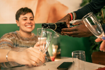 Close-up of pouring champagne into a glass for a celebratory toast. Friends sharing sparkling wine at a restaurant or home party for a New Year's Eve or holiday dinner.