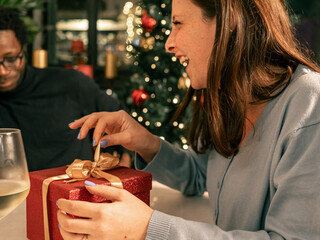A happy woman laughing with joy while opening a Christmas gift. A candid moment of surprise and...