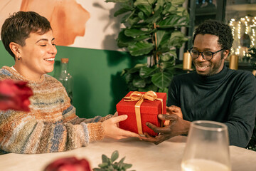 Happy diverse couple sharing an intimate moment during a Christmas gift exchange. Love, connection,...