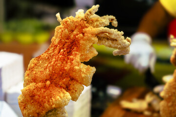 Close-up of crispy, golden-brown fried snack sprinkled with red chili powder. Vibrant texture and seasoning contrast with softly blurred background suggesting active food preparation scene.