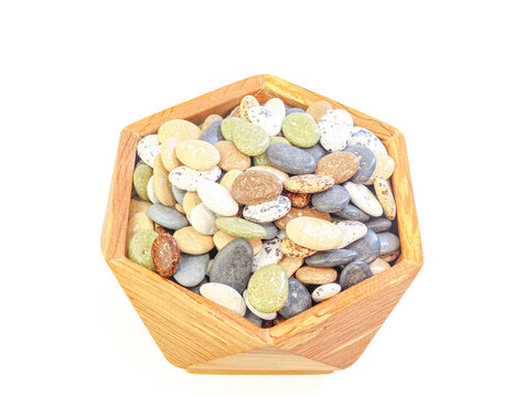Mixed colorful dried beans in various shapes and shades&mdash;green, brown, white, and gray&mdash;are arranged in a hexagonal wooden bowl. A staple in vegetarian diets, these legumes are high