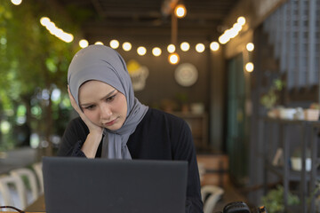 muslim women wear hijab sitting at work using a laptop and headache. Migraines, dizziness from...