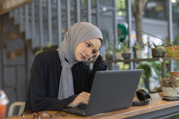muslim women wear hijab sitting at work using a laptop and headache. Migraines, dizziness from...