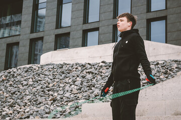 Young man with jump rope and earbuds stands focused in an urban setting with modern architecture...