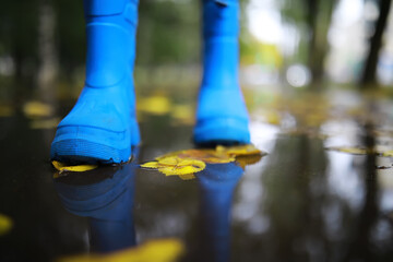 legs of child in blue rubber boots jumping in the autumn puddles