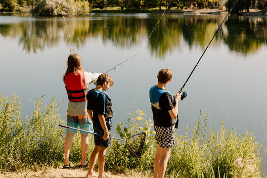 Kids fishing by calm lake in summer with life jackets on