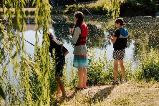 Three preteens fishing lakeside under tree branches