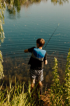 Young fisherman casting line in calm lake on sunny day
