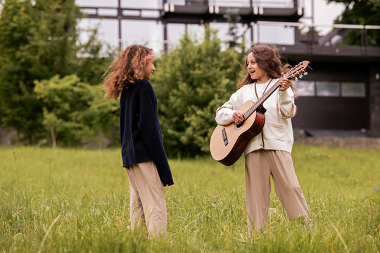 Two twin girls with curly hair playing on a guitar and having fun