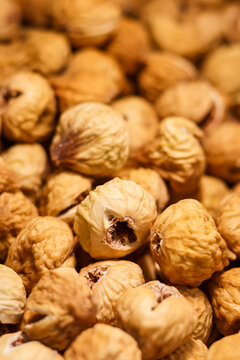 A tightly packed pile of dried figs fills the frame with wrinkled textures and warm golden-brown tones. Captured in macro detail, the image reveals natural cracks, folds, and a fine sugary coating