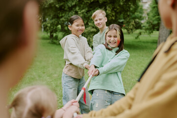 Group of multiethnic children playing tug of war outdoors in park, smiling and pulling rope...