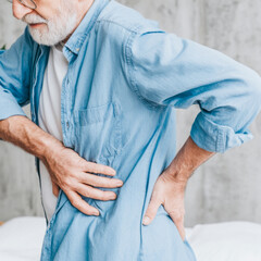 Old man experiencing lower back pain indoors with a pained expression and cozy atmosphere