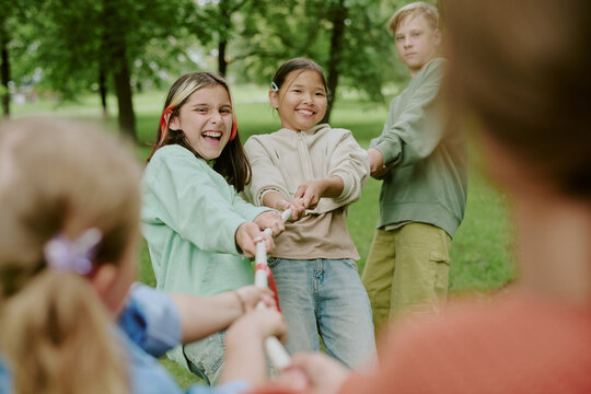 Group of multiethnic children playing tug of war outdoors in park, smiling and pulling rope together, participating in team building activity
