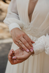 The bride in a white embroidered dress holds the sleeve of her dress with her hand and shows off...